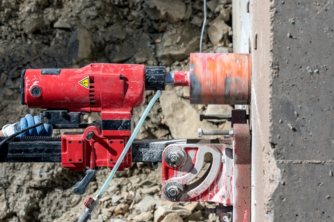 Worker is drilling to concrete wall with core drill machine. Core drills used in metal are called annular cutters. Core drills used for concrete and hard rock generally use industrial diamond grit.